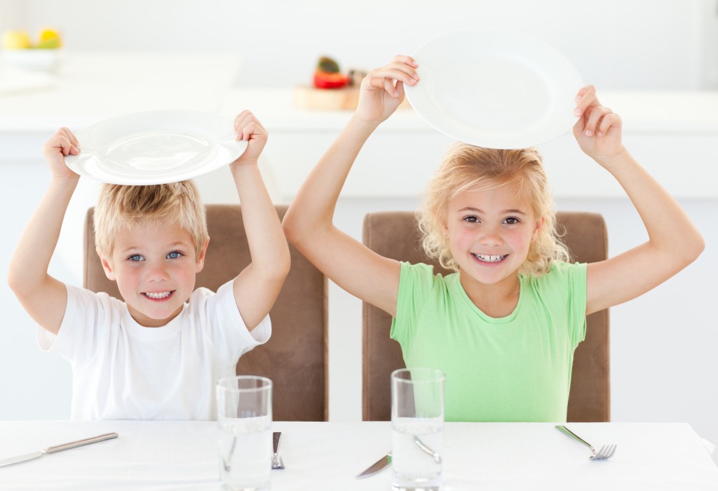Funny brother and sister asking for their lunch raising their plates in the kitchen